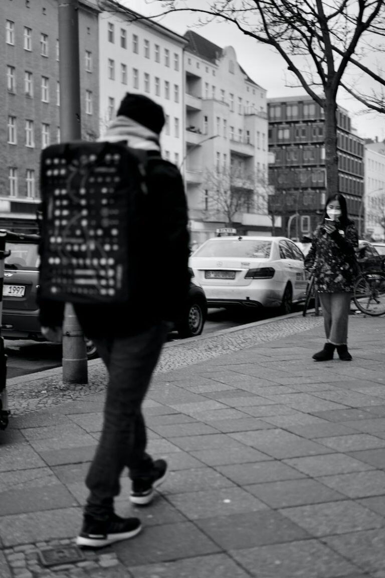 man in black jacket and pants standing on sidewalk during daytime